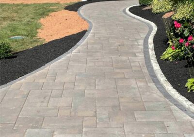 Curved stone pathway bordered by black mulch and colorful flowers, showcasing McIsaac Lawncare's landscaping craftsmanship and outdoor transformation.