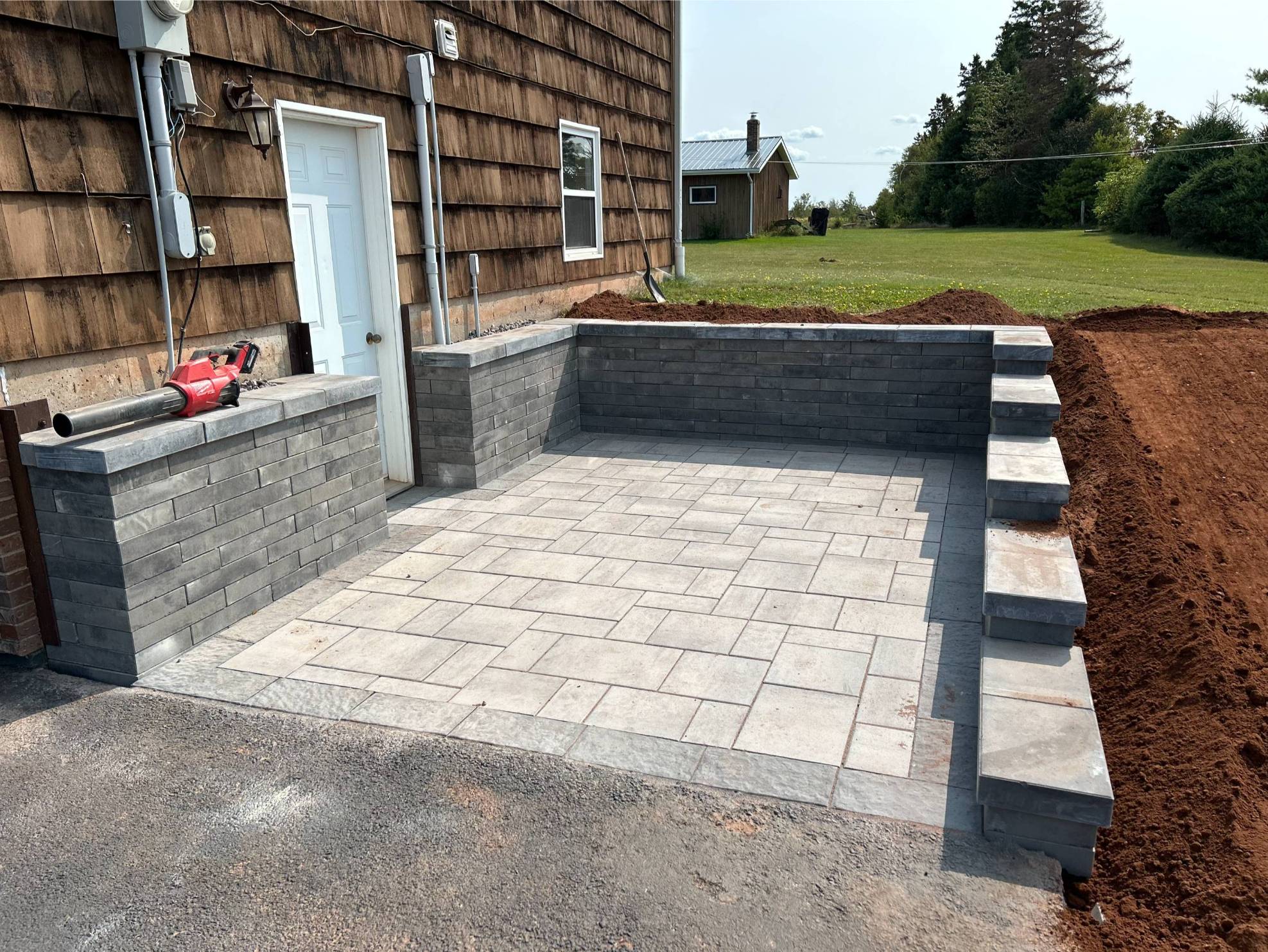 Custom patio installation featuring gray pavers, surrounding walls, and unfinished landscaping, designed to enhance outdoor living spaces.