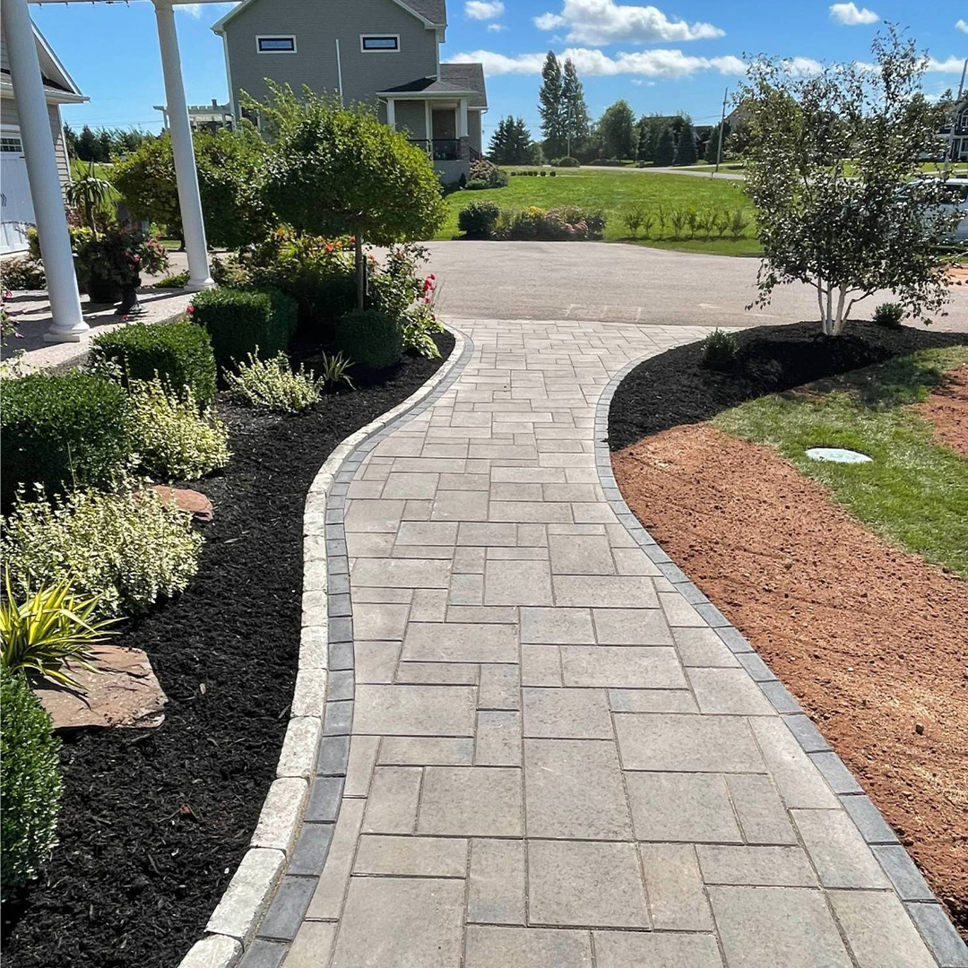 Curved stone pathway bordered by lush greenery and mulch, showcasing professional hardscaping by McIsaac Lawncare for enhanced outdoor aesthetics.