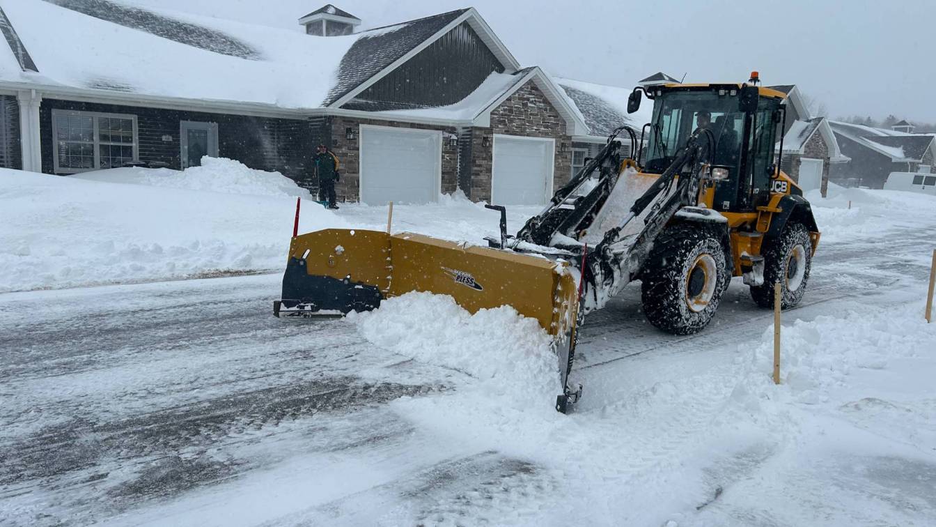 Snow plow clearing residential driveway in winter, surrounded by deep snow, showcasing professional snow removal services by McIsaac Lawncare.