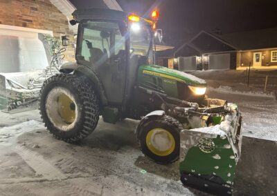 Tractor with snowplow attachment clearing snow at night, showcasing McIsaac Lawncare's winter landscaping services.