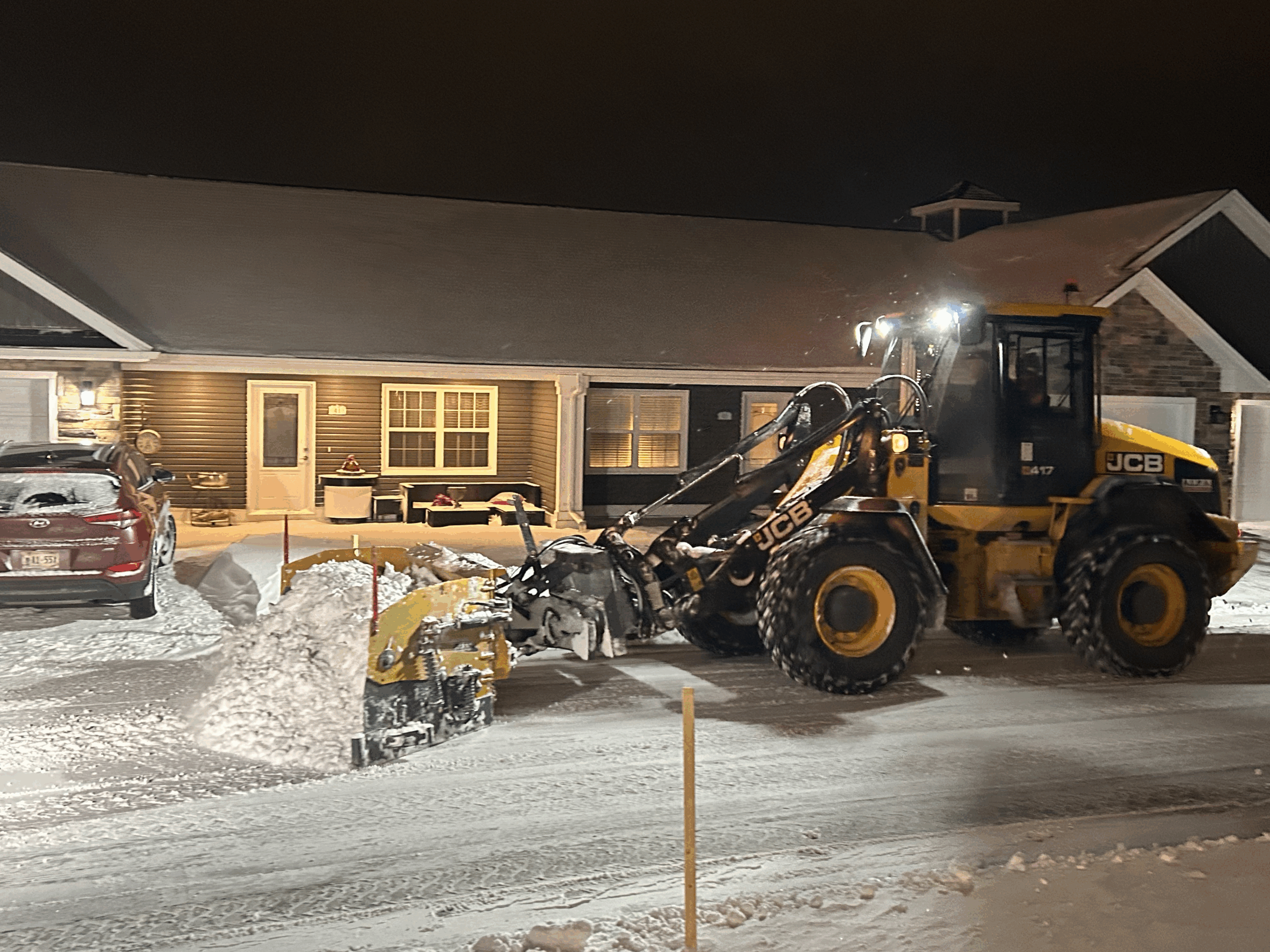 Snow removal equipment clearing driveway at night, residential home in background, showcasing McIsaac Lawncare's efficient snow management services.