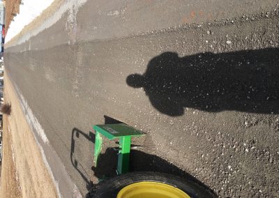 Shadow of a person next to a green lawn care machine on a gravel path, illustrating landscaping equipment used for outdoor transformations.