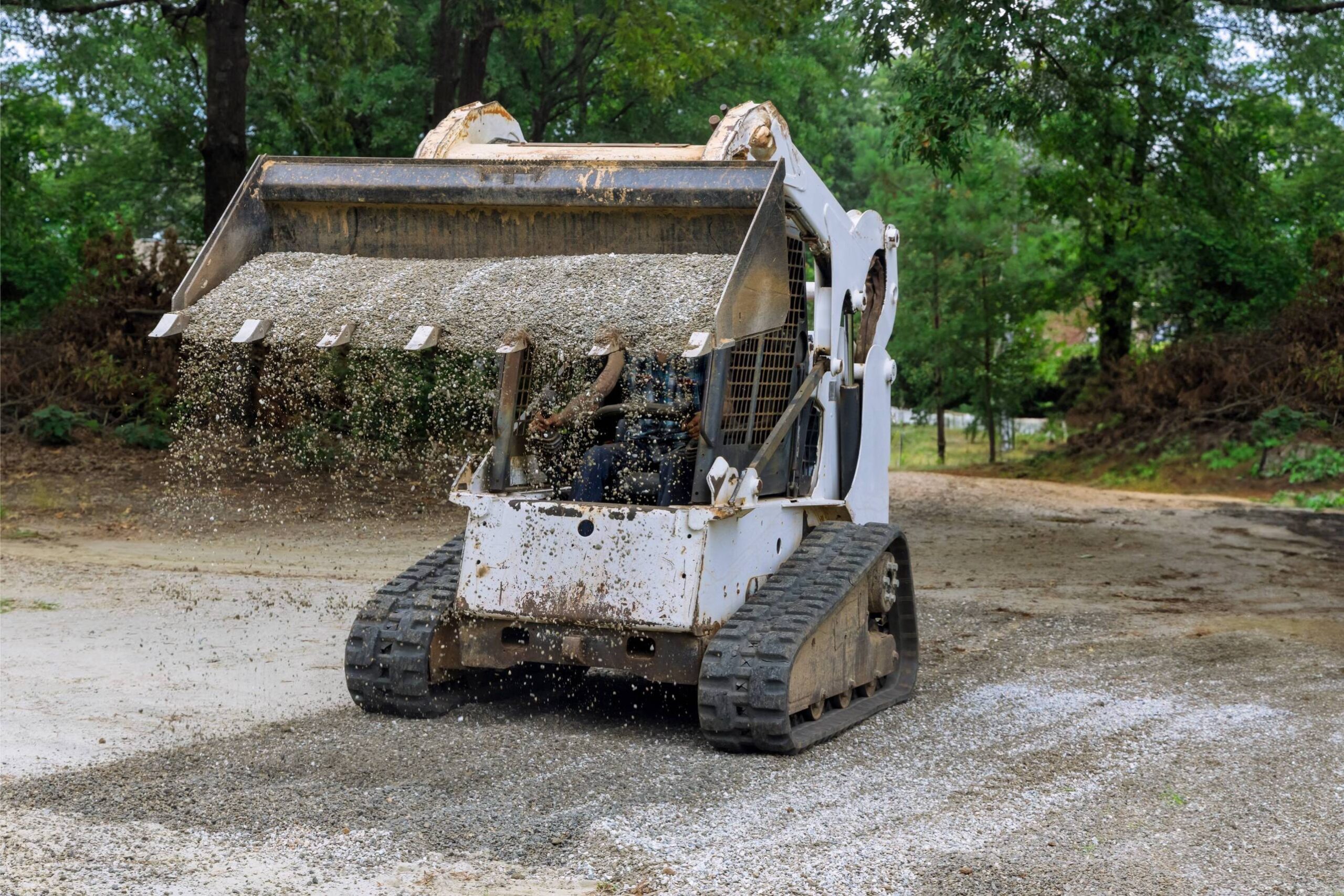 Bobcat mini-loader spreading gravel on a construction site, illustrating excavation and driveway installation services by McIsaac Lawncare.