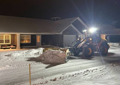 Snow removal equipment clearing driveway at night, showcasing effective winter landscaping service by McIsaac Lawncare.