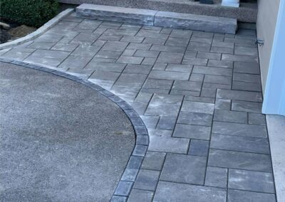 Paved walkway featuring a curved design and textured stone pattern, showcasing McIsaac Lawncare's quality craftsmanship in outdoor landscaping.