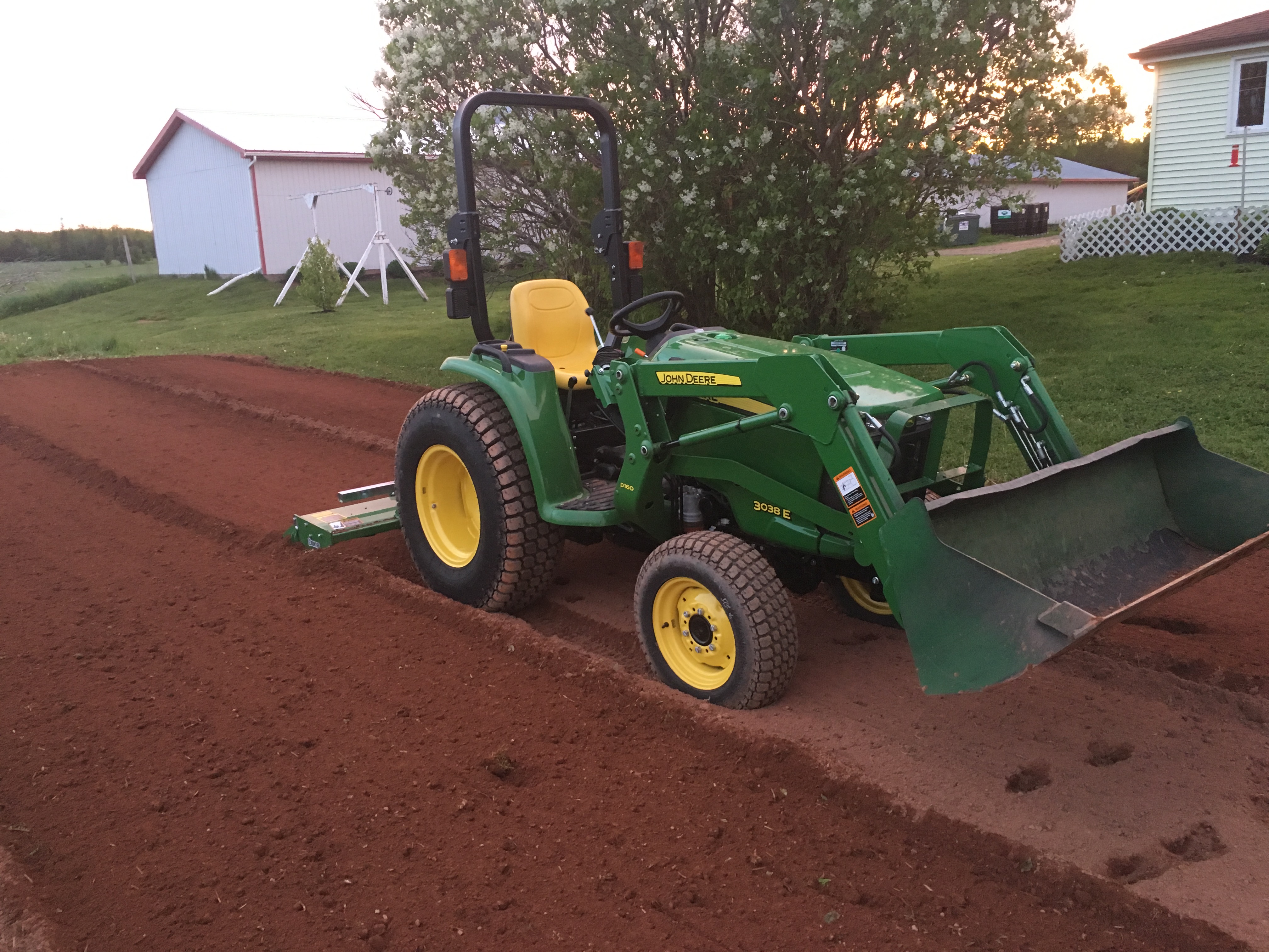 John Deere tractor preparing soil for hydroseeding, with freshly tilled rows in a residential yard setting, emphasizing expert site preparation for lawn establishment.