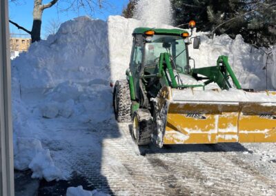 Tractor with front loader clearing snow from driveway, showcasing winter landscaping services by McIsaac Lawncare.