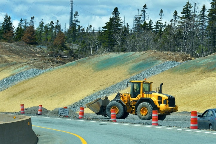Excavator working on a hydroseeding project, surrounded by construction barriers and freshly prepared soil in Montague area.