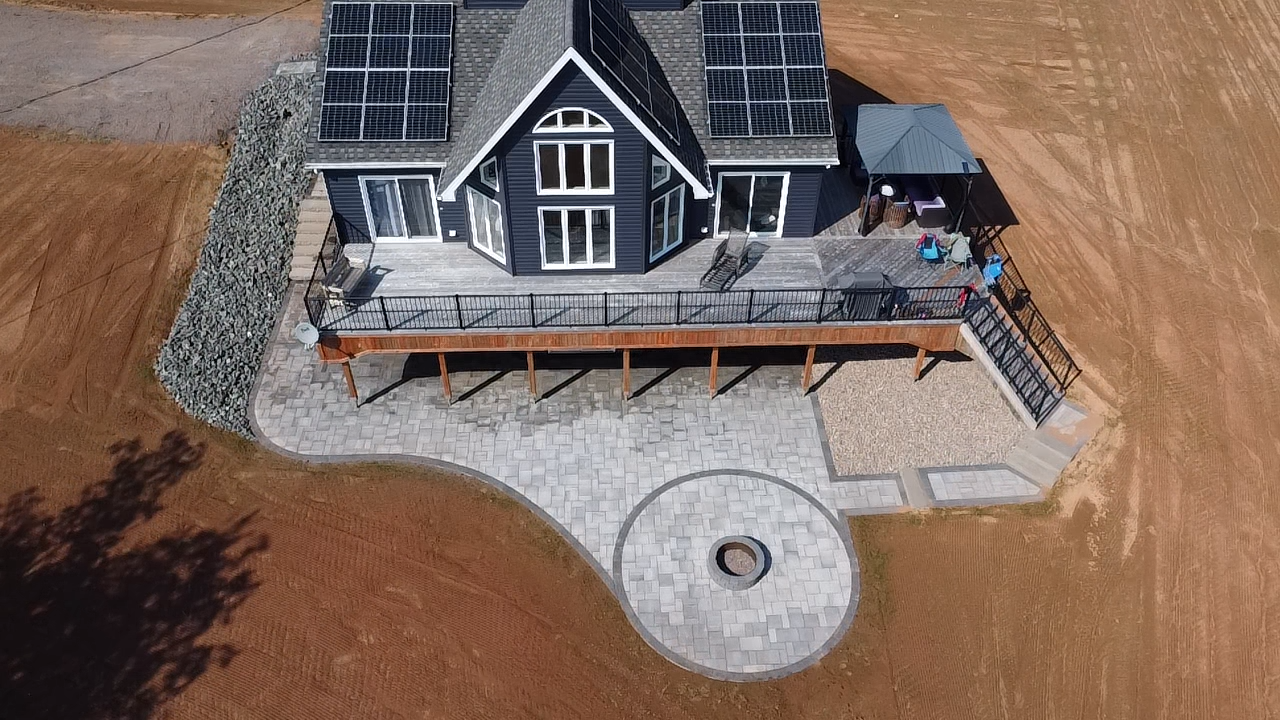 Aerial view of a modern home with solar panels, featuring a custom paver patio, circular fire pit, and outdoor seating area, highlighting hardscaping design by McIsaac Lawncare.