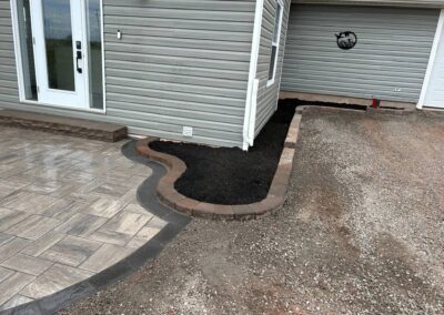 Newly landscaped outdoor area featuring a curved stone border, fresh mulch, and a textured patio, showcasing McIsaac Lawncare's craftsmanship in transforming backyard spaces.