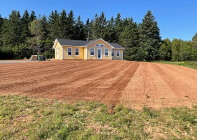 Lawn transformation project featuring freshly tilled soil and a yellow house surrounded by trees, showcasing McIsaac Lawncare's landscaping expertise.