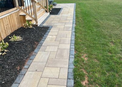 Paved walkway leading to a wooden deck, bordered by black mulch and green grass, showcasing McIsaac Lawncare's landscaping craftsmanship and outdoor transformation.