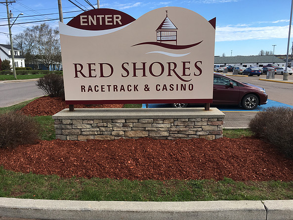Sign for Red Shores Racetrack & Casino with stone base and landscaped flower beds, featuring the word "ENTER" prominently at the top.