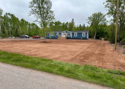 Newly landscaped backyard with freshly graded soil, blue house in background, and trees, showcasing McIsaac Lawncare's outdoor transformation services.