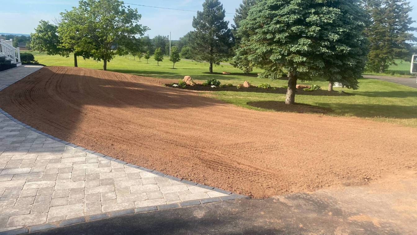 Lawn preparation area with freshly graded soil, surrounded by trees and landscaped features, ready for lawn seeding and yard prep services by McIsaac Lawncare.