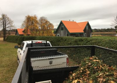 Truck and trailer parked in a landscaped yard with a wooden house featuring an orange roof, showcasing McIsaac Lawncare's landscaping services and outdoor transformations.