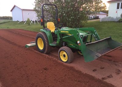 Green tractor preparing soil for landscaping project in residential backyard.