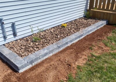 Landscaped area featuring a stone border with decorative gravel and small plants, showcasing McIsaac Lawncare's outdoor transformation expertise.