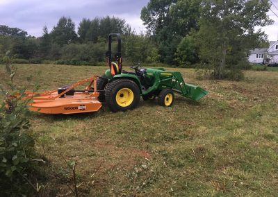 Lawn care equipment, including a green tractor with a yellow mower attachment, in a cleared outdoor space, showcasing McIsaac Lawncare's landscaping services and expertise in transforming overgrown lots.