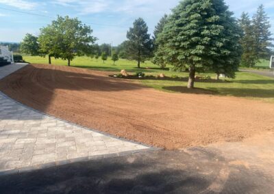 Lawn transformation project featuring freshly graded soil in a spacious yard with trees and a stone patio edge, showcasing McIsaac Lawncare's landscaping expertise.
