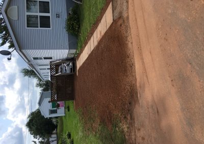 Landscaped backyard transformation featuring a freshly prepared area with a stone pathway leading to a wooden deck, showcasing McIsaac Lawncare's quality craftsmanship in outdoor spaces.