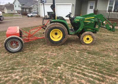 Green John Deere tractor with attached red lawn care equipment on a grassy residential lawn, showcasing McIsaac Lawncare's landscaping services and equipment used for outdoor transformations.
