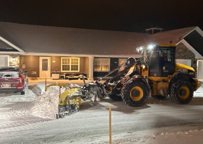 Loader clearing snow in front of residential property at night, showcasing winter landscaping maintenance services by McIsaac Lawncare.