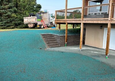 Landscaped outdoor space with blue gravel, wooden deck, and steps leading to a garage, showcasing McIsaac Lawncare's recent project in outdoor transformation.