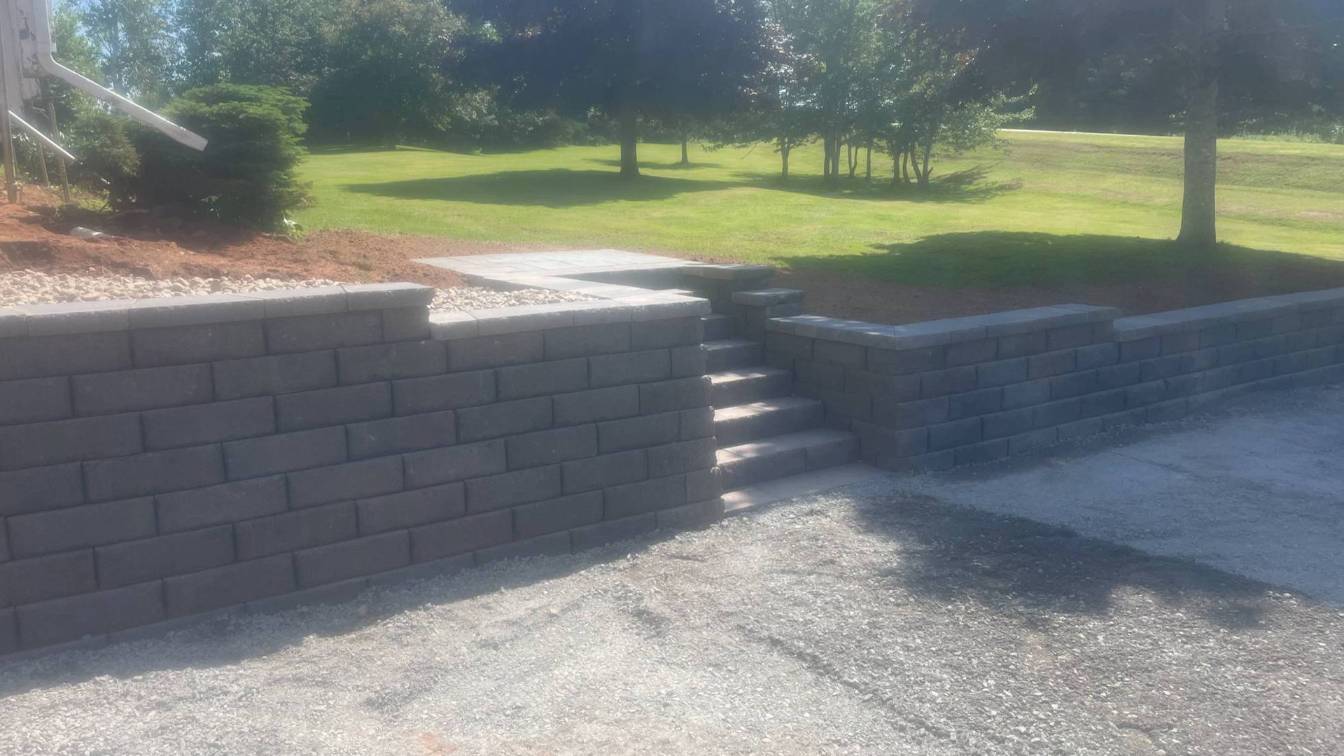 Retaining wall built with concrete blocks, featuring steps leading to a landscaped area with grass and trees, showcasing hardscaping solutions for outdoor spaces.