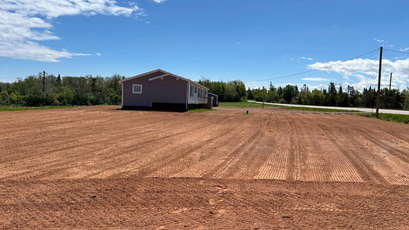 Excavated land with freshly graded soil and a residential building, showcasing site preparation for landscaping and construction projects.
