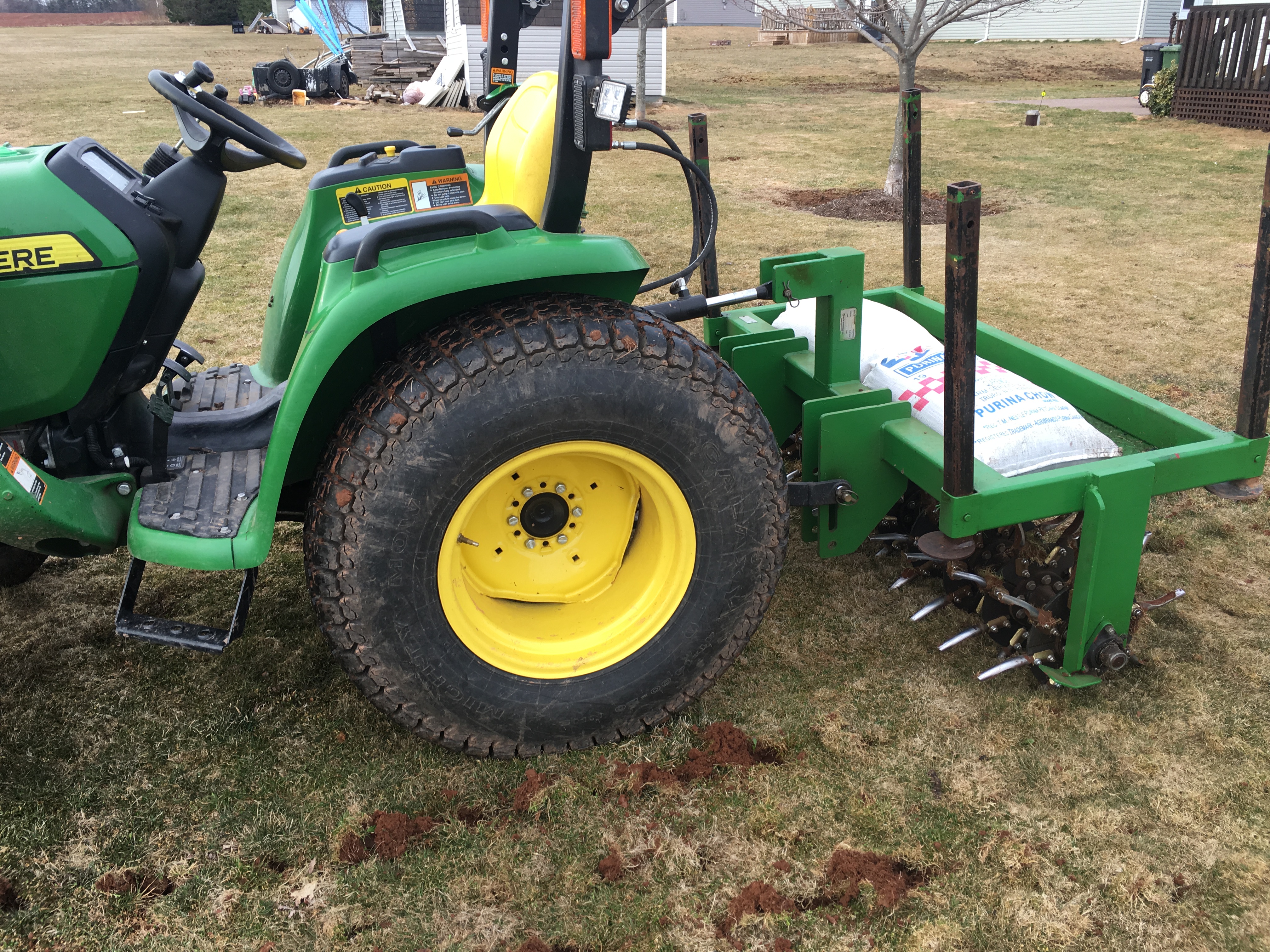 John Deere tractor with aerator attachment and fertilizer bag, positioned on prepared lawn for effective seeding and soil preparation.