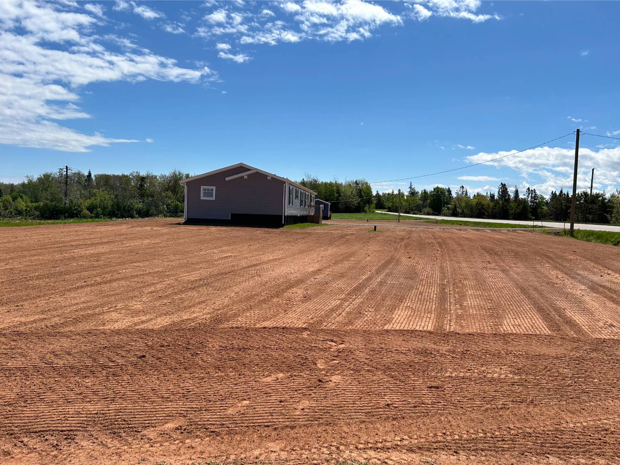 Excavated lot preparation with freshly graded soil, adjacent to a residential building, under a clear blue sky in Prince Edward Island.