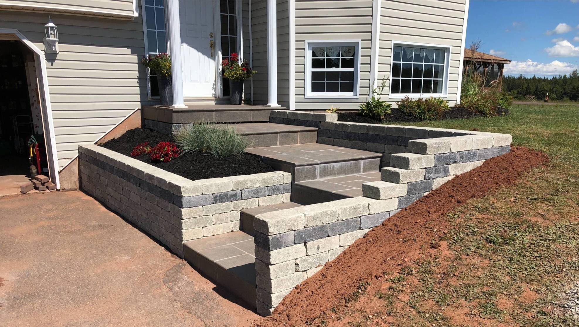 Paver steps and retaining wall leading to a home entrance, showcasing expert hardscaping design with durable materials and landscaping elements.