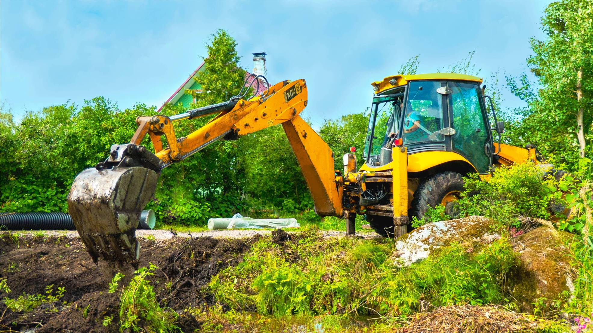 Excavator with bucket digging in a field surrounded by greenery, illustrating land clearing for excavation and landscaping services.