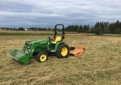 Tractor on a grassy field with a mower attachment, showcasing McIsaac Lawncare's landscaping equipment for outdoor transformations.
