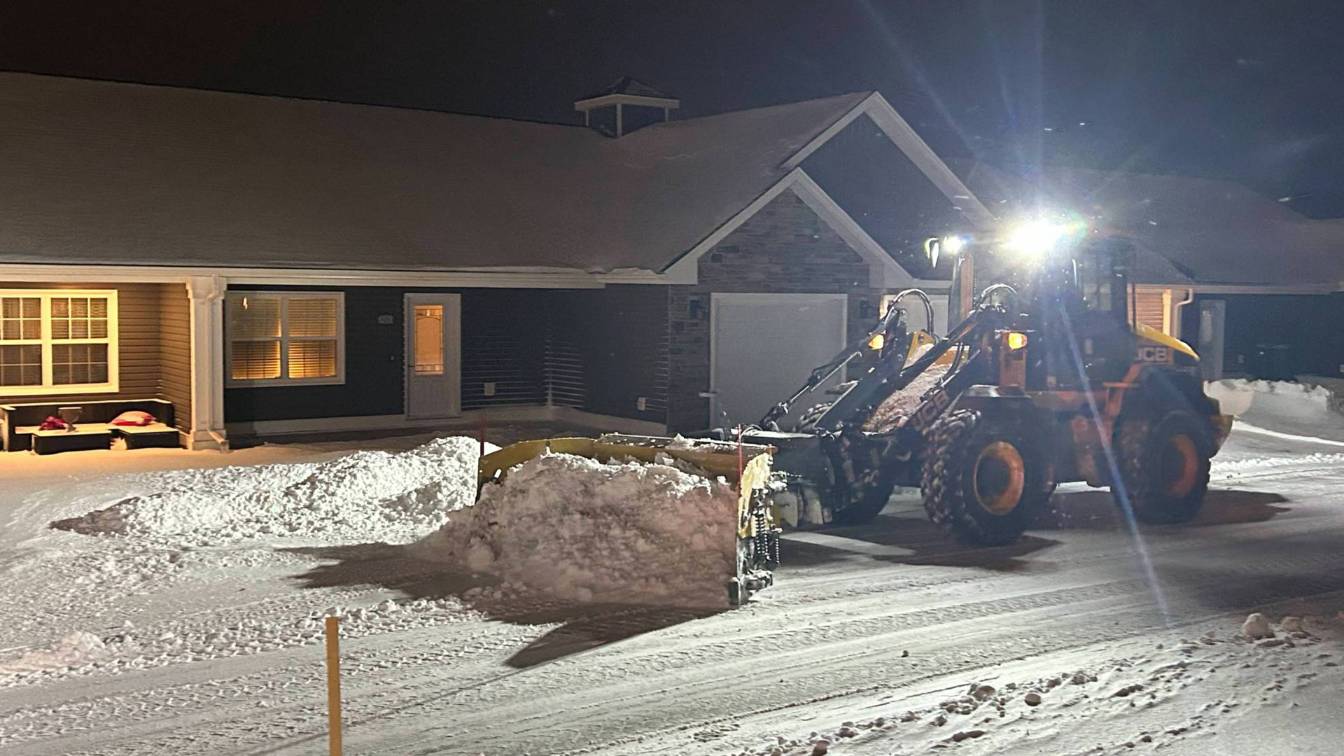 Loader clearing snow from residential driveway at night, illuminated by headlights, emphasizing snow removal services for safety and accessibility.