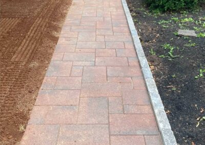 Paved walkway showcasing quality craftsmanship by McIsaac Lawncare, surrounded by freshly prepared soil and landscaped areas.