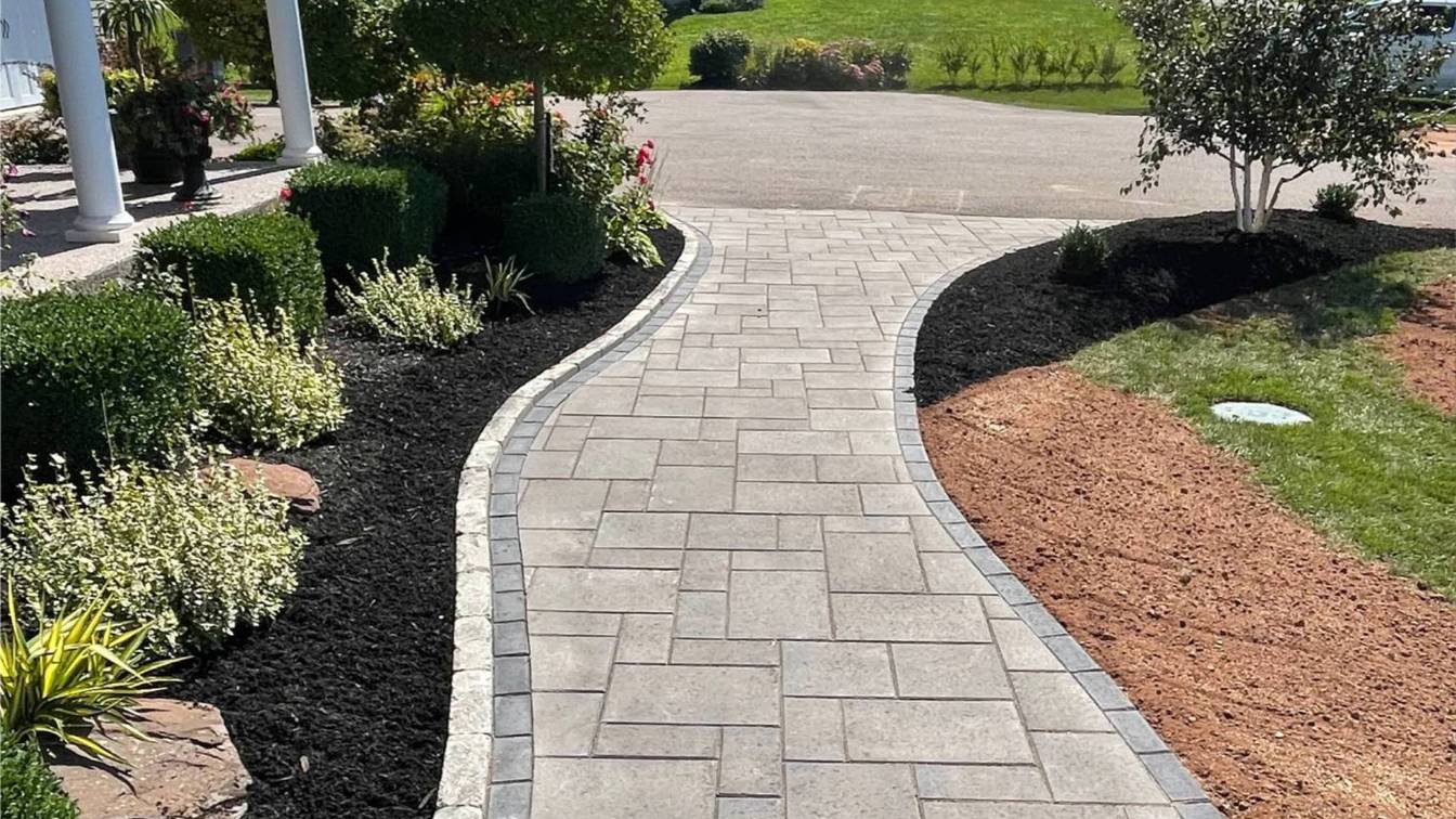 Curved paver walkway bordered by lush greenery and black mulch, enhancing outdoor space aesthetics and functionality.