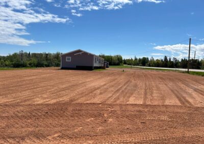 Landscaped yard with freshly graded soil and a nearby house, showcasing preparation for outdoor transformation by McIsaac Lawncare.