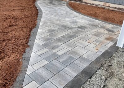 Paved walkway with gray stone tiles leading through a landscaped area, showcasing McIsaac Lawncare's craftsmanship in outdoor transformations.