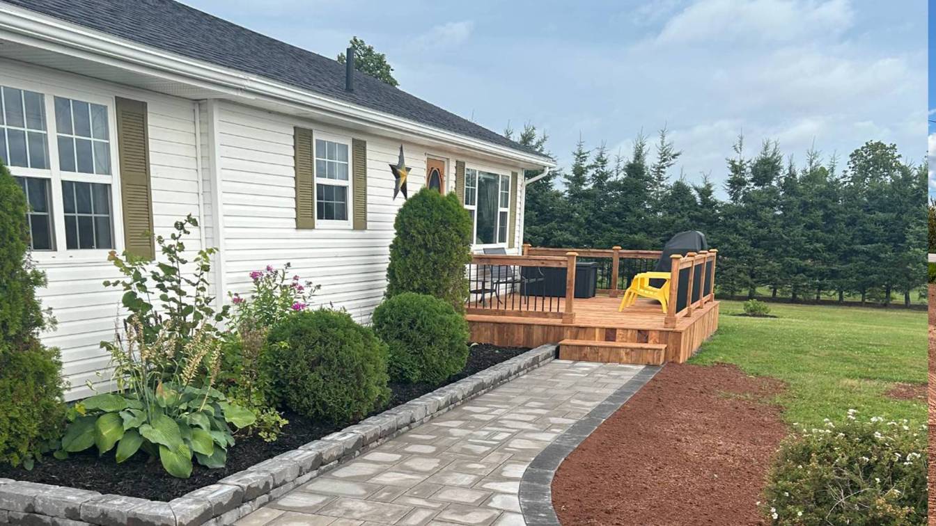 Patio area featuring a well-designed paver walkway, landscaped with bushes and flowers, adjacent to a wooden deck, enhancing outdoor space for gatherings and relaxation.