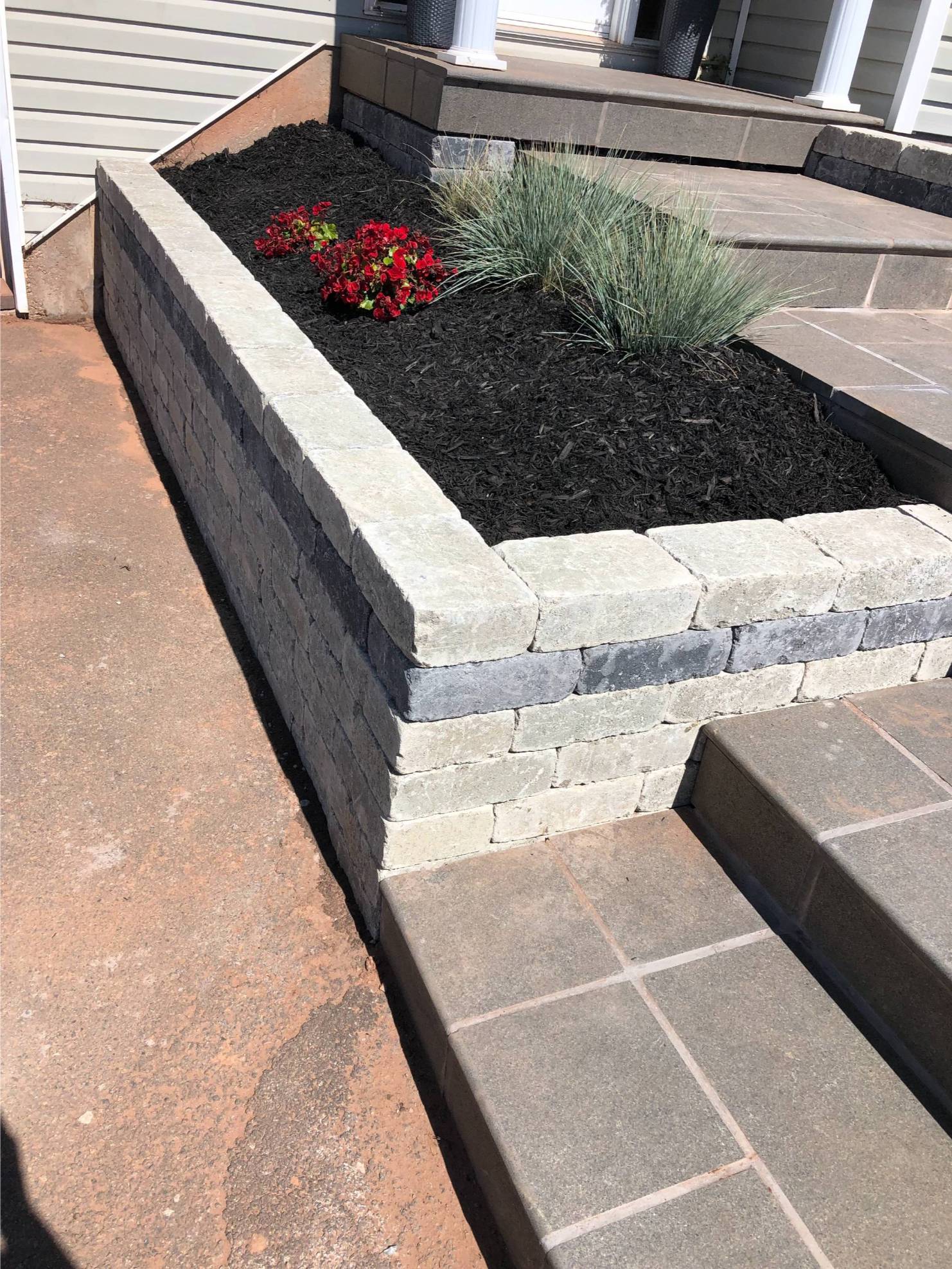 Custom retaining wall with stacked stone, vibrant red flowers, and ornamental grasses, enhancing outdoor space and curb appeal.