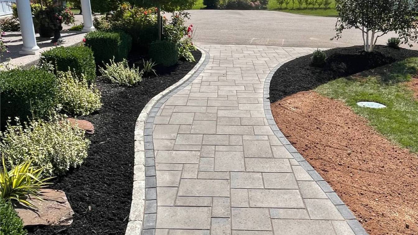 Curved paver walkway bordered by lush greenery and black mulch, showcasing durable hardscaping design for enhanced outdoor aesthetics.