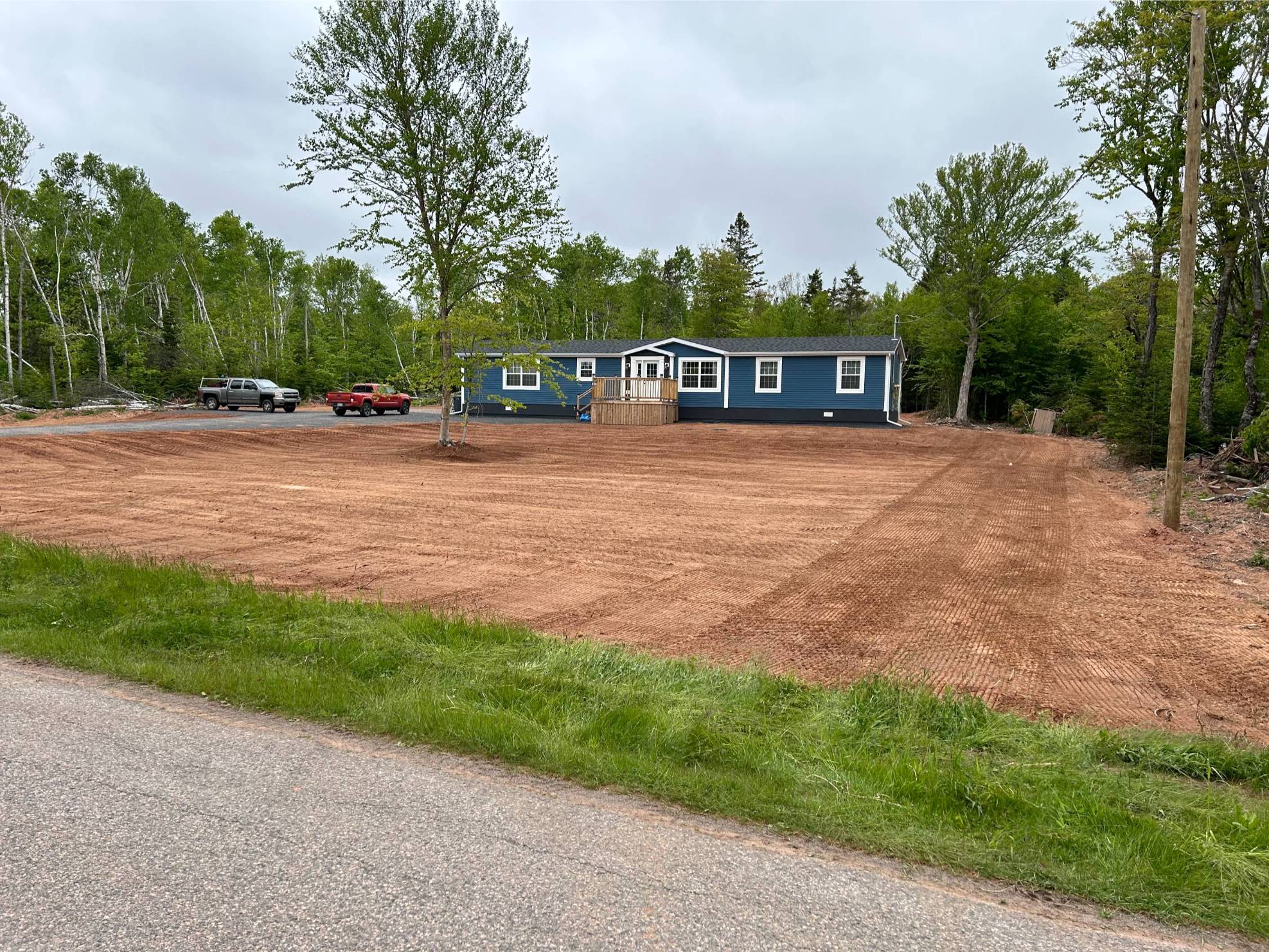 Newly excavated lot with a blue home, parked vehicles, and surrounding trees in eastern Prince Edward Island, showcasing McIsaac Lawncare's outdoor services.