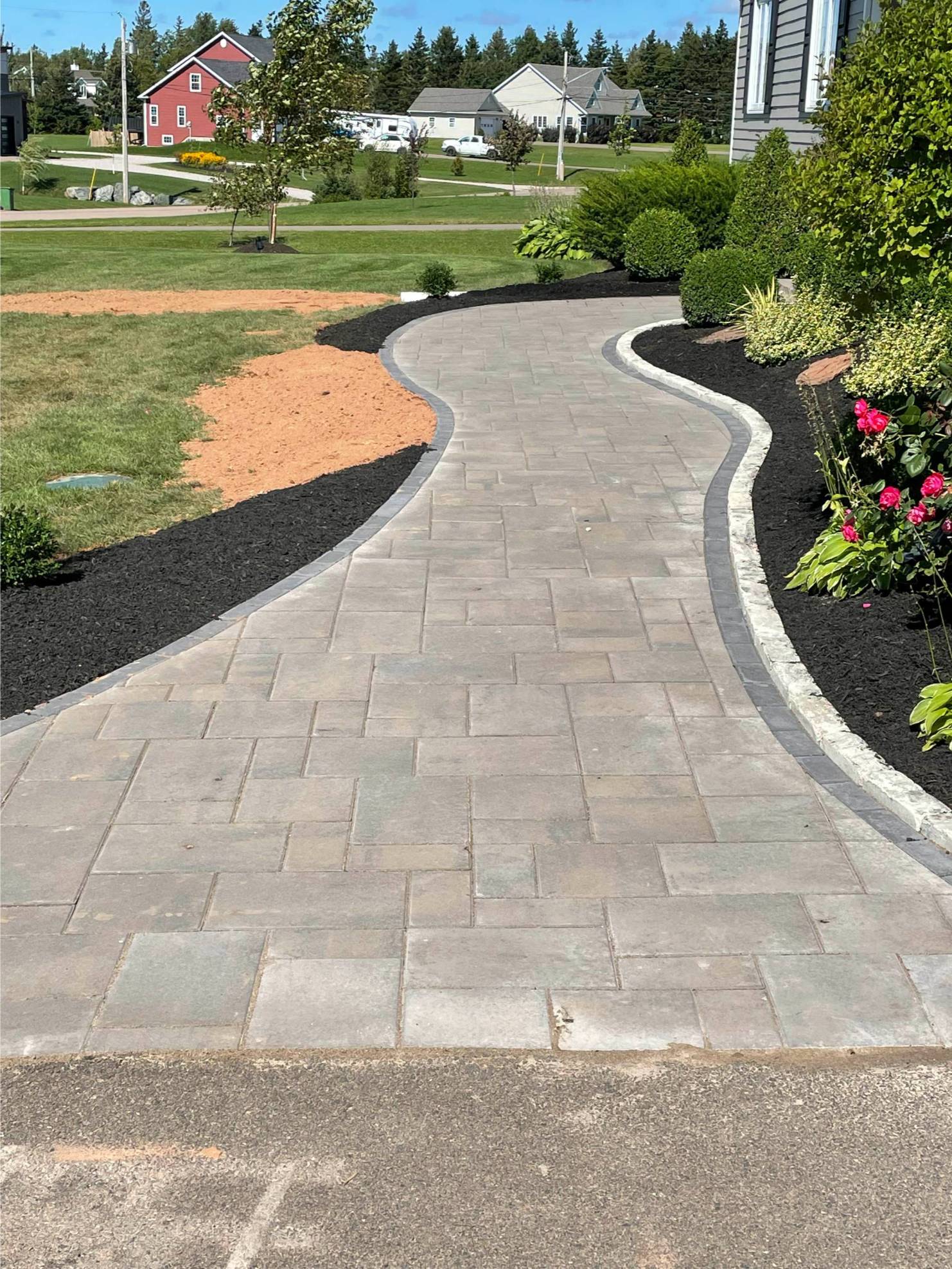 Curved stone walkway bordered by black mulch and vibrant flowers, enhancing outdoor space aesthetics for hardscaping services by McIsaac Lawncare.