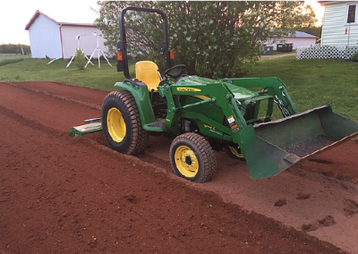 Tractor tilling soil in a residential backyard, preparing for landscaping and outdoor transformations by McIsaac Lawncare.