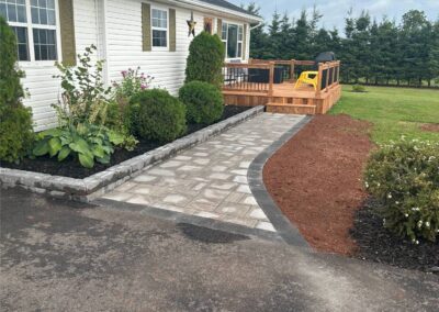 Landscaped pathway with stone pavers leading to a wooden deck, surrounded by greenery and freshly mulched areas, showcasing McIsaac Lawncare's outdoor transformation expertise.