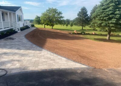 Landscaped backyard transformation featuring a newly installed paver patio and prepared soil area for planting, showcasing McIsaac Lawncare's craftsmanship and outdoor improvement services.