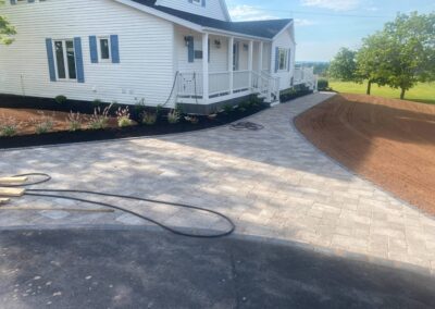 Newly paved stone pathway leading to a house, featuring landscaped flower beds and a freshly graded lawn area, showcasing McIsaac Lawncare's quality craftsmanship in outdoor transformations.